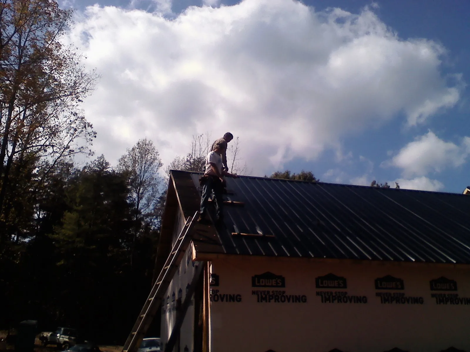 Roofer fastening dark metal panels high against a cloudy sky, from a Roof Inspection job in Topeka