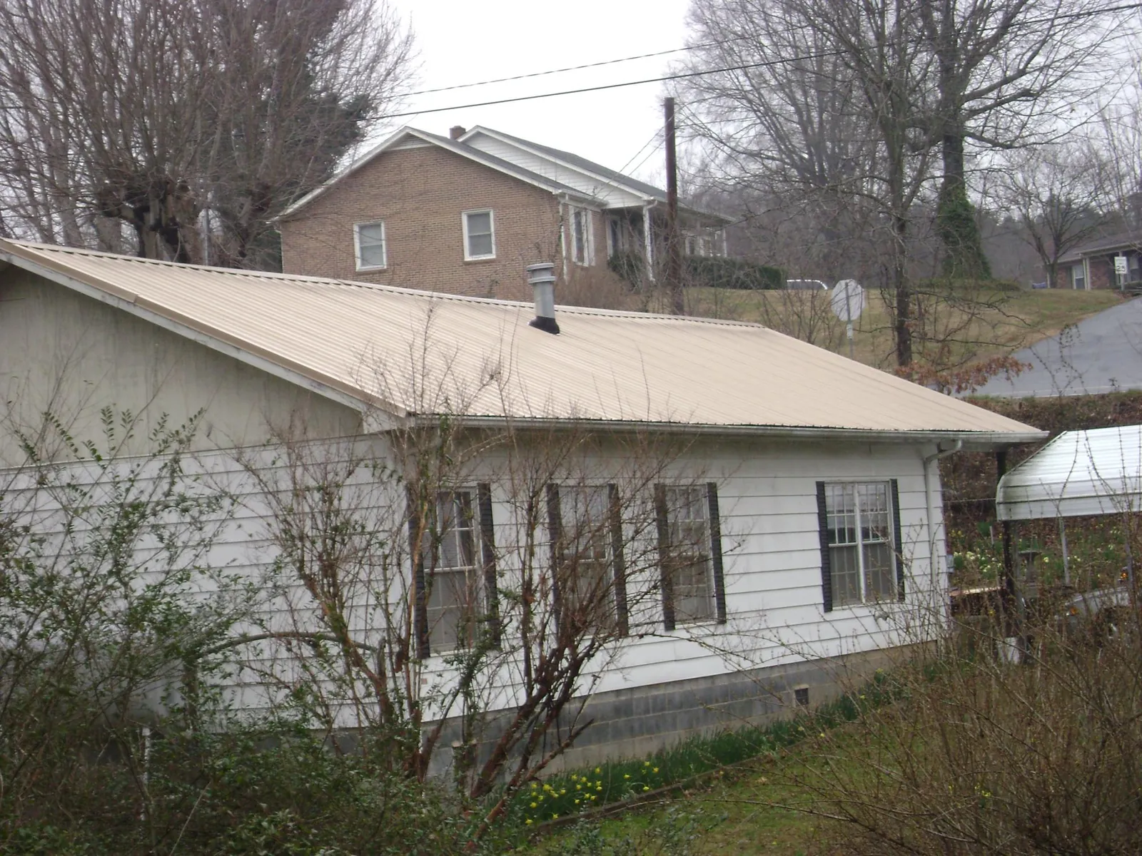 Tan metal roof on a white sided house set into a hillside — Commercial Roofing by Roofing Brothers in Topeka